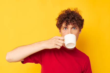 cute red-haired guy posing with a white mug and in the hands of a drink yellow background unaltered