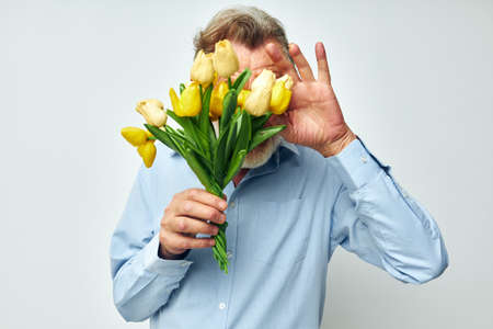 Portrait of happy senior man a bouquet of flowers with glasses as a gift light backgroundの写真素材