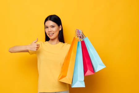 woman with Asian appearance in a yellow T-shirt with multicolored shopping bags yellow background unalteredの写真素材