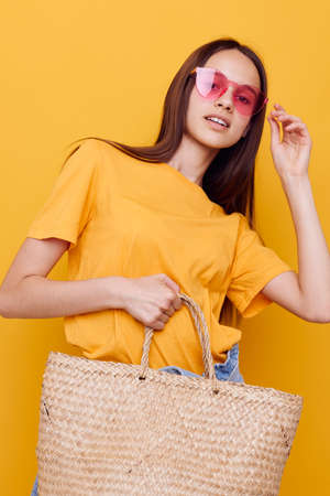 young woman wicker bag in hand pink glasses yellow backgroundの写真素材