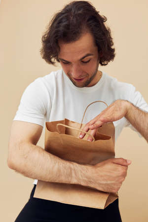 Cheerful man in a white T-shirt with paper bag beige background