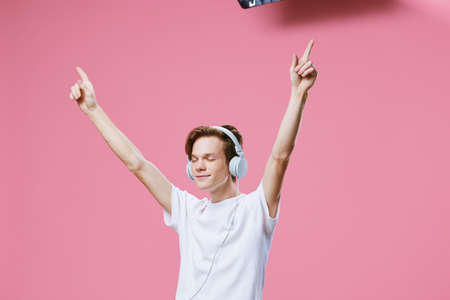 happy young man in a white t-shirt emotionally and joyfully listens to music in bright headphones...
