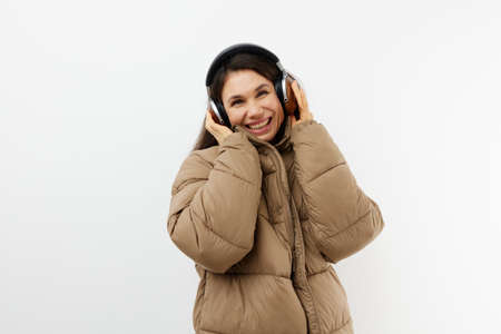beautiful happy brunette listening to music in headphones standing in a warm winter stylish jacket...