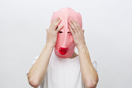 a man in a funny pink mask covers his face with his handsの写真素材