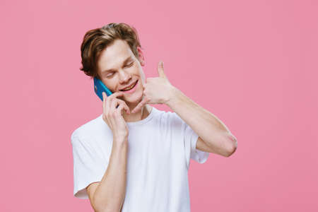 handsome, pleasant, smiling young man holds a smartphone near his ear and shows a call me gesture