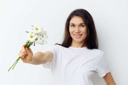portrait of a cute, beautiful, pleasant woman with black hair in a white clean t-shirt, holding a...