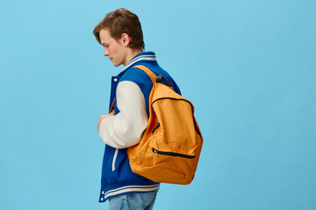 student with a backpack on his shoulder posing on a blue background