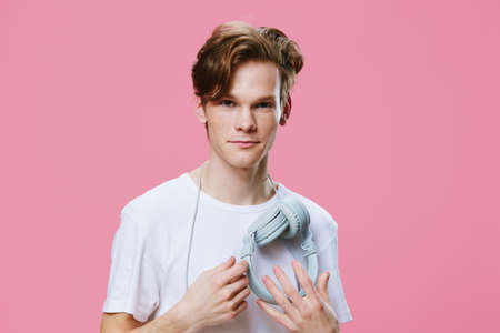 beautiful young man in a white T-shirt on a pink background with headphones around his neck smiling cutely at the cameraの写真素材