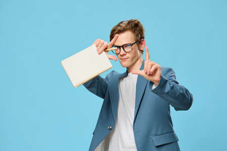 a handsome young man in a suit for office work is wearing glasses and with a notebook in his hands,...