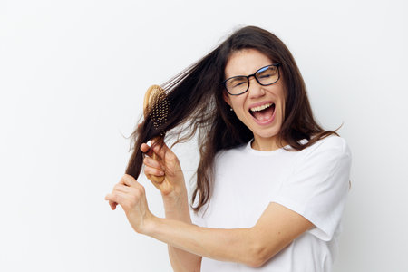 portrait of a beautiful woman in a light T-shirt trying to comb her long tangled hair with a wooden comb and screaming in painの写真素材
