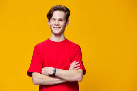 joyful guy in a red T-shirt with a fitness bracelet posing with arms folded on his chest