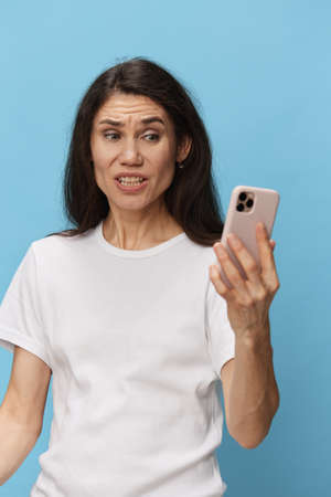 a shocked emotional woman with long hair stands in a white T-shirt on a light blue background and...