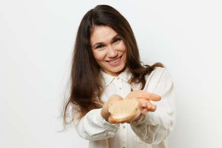 a beautiful woman holds a comb in her hands and holds it out to the camera while standing in a white shirt on a light backgroundの写真素材