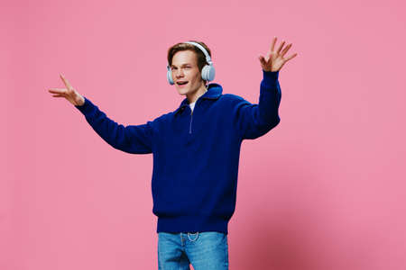 happy attractive young man rejoices listening to music in headphones raising his hands up. Studio horizontal photo with space for advertising textの写真素材