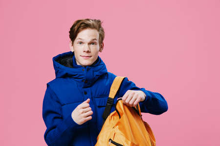 a handsome young attractive man with red hair stands in a dark-colored winter outerwear looking at...