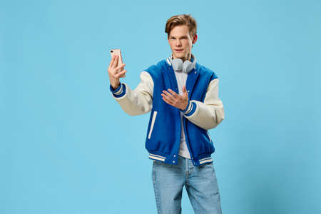 handsome stylish young man takes a selfie on the phone with his arm outstretched while standing with...