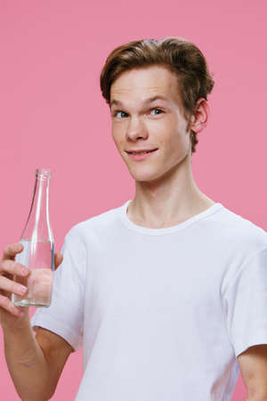 joyful, happy guy stands with a glass bottle of water in his hands on a pink backgroundの写真素材