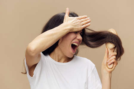 beautiful, cute, attractive middle-aged brunette combs her long hair with a wooden comb while standing in a white poppy and shouts covering her face with her handの写真素材