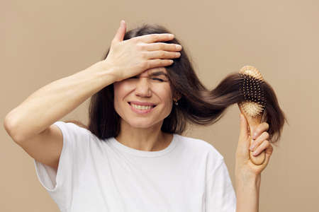 beautiful, cute, attractive middle-aged brunette combs her long hair with a wooden comb while standing in a white poppy and shouts covering her face with her handの写真素材