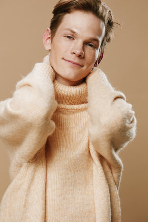 close portrait of a handsome young guy with freckles in a beige textured high neck sweater raising his elbows to the cameraの写真素材
