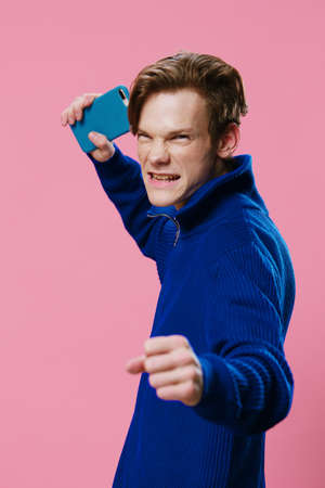 an active, joyful man posing, raising a phone in a blue case in his hand and clenching his hand into a fist. photo with space for textの写真素材