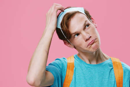 comical, funny portrait of a student guy who put on a medical mask on his head, and thoughtfully combs his hair. Themes of study during a pandemicの写真素材