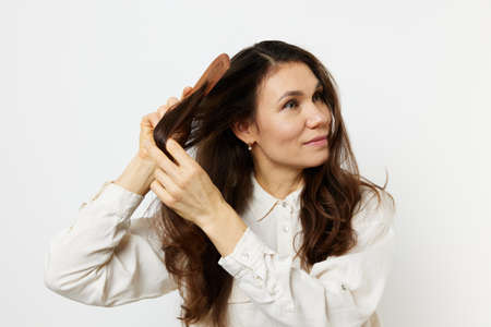 joyful happy woman combing her hair with a wooden comb smiling joyfully. Horizontal photo on a light backgroundの写真素材