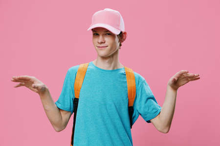 funny guy funny stretches his hands forward while standing in a blue t-shirt and pink cap. Studio photo on a pink background with empty space for textの写真素材