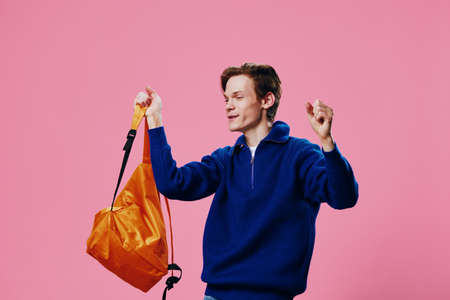 a happy joyful guy with a bright orange backpack in his hand shouts joyfully while raising his bag...