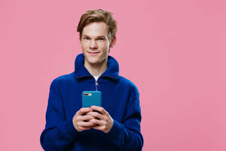 a handsome red-haired guy stands with a phone in a blue case in his hands and smiles cutely at the cameraの写真素材