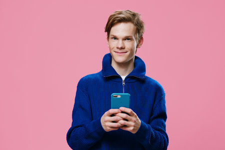 a handsome red-haired guy stands with a phone in a blue case in his hands and smiles cutely at the...