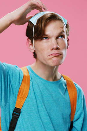 comical, funny portrait of a student guy who put on a medical mask on his head, and thoughtfully...