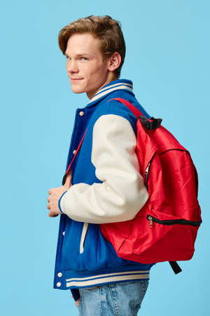 young man with a red backpack on his back. Studio photography, plain background with space for textの写真素材