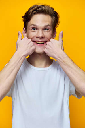 portrait of a happy guy in a white t-shirt posing emotionally with fingers near his faceの写真素材