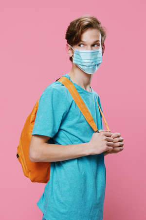 portrait of a student guy with a medical mask on his face and with a backpack on his back on a pink...