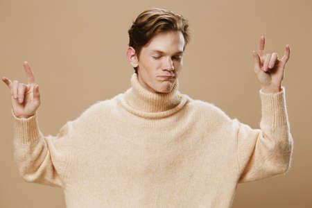 handsome guy in a beige sweater shows a rock sign with his handsの写真素材