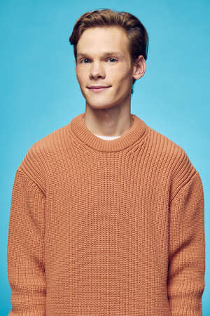cute, handsome guy in an orange sweater stands on a blue background
