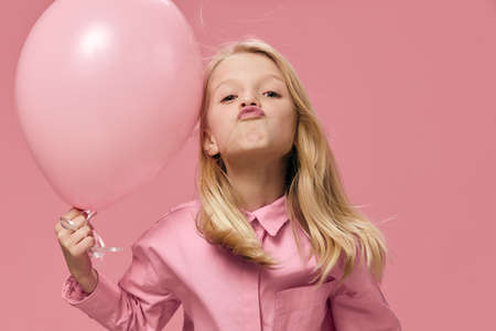 a happy, joyful school-age girl stands on a pink background with a big balloon with her lips folded in a kiss. Horizontal photo with blank space for advertising layout insertの写真素材