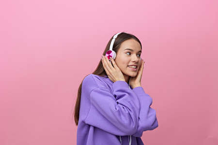 a cheerful, happy woman in a purple tracksuit enjoys music holding headphones with her hands on both...
