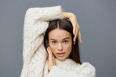 a close horizontal photo of a beautiful, charming woman in a white sweater standing on a gray...