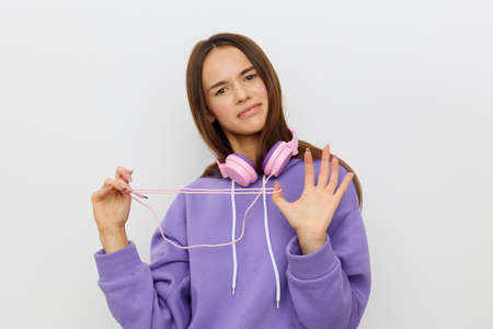 a stunned woman stands on a white background in a purple tracksuit with an uncomprehending look trying to untangle the headphone wireの写真素材