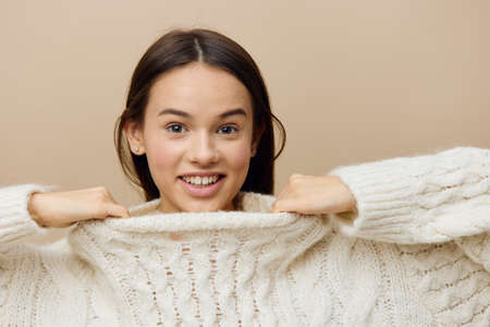 a modest woman stands in a half turn on a light background playfully looks forward smiling cheerfully stretching the neck of the sweaterの写真素材