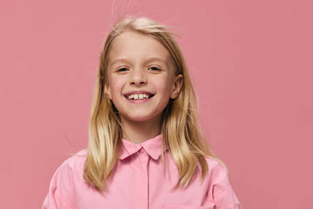 horizontal portrait of a school-age blonde girl in a pink shirt, standing against a one-time background and smiling broadly looking at the camera. Studio photo with empty space for advertising mockupの写真素材