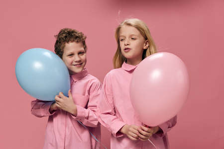 beautiful, happy children boy and girl stand on a pink background holding pink and blue balloons in their handsの写真素材