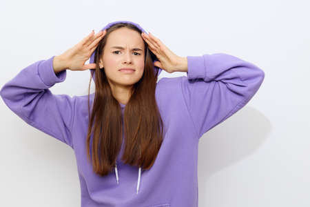 an interested woman is standing on a white background in a purple tracksuit wearing a hood on her...