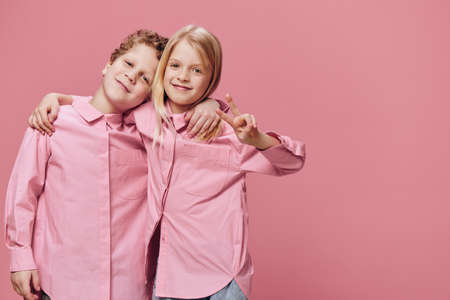 cute beautiful children stand in pink clothes on a pink background with their hands on each others shouldersの写真素材