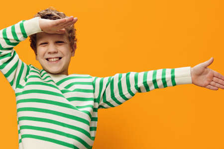 horizontal portrait of a cute curly boy of school age in a striped long-sleeved t-shirt on an orange backgroundの写真素材