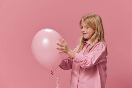a beautiful, happy girl in a pink shirt stands on a pink background and smiling broadly at the...