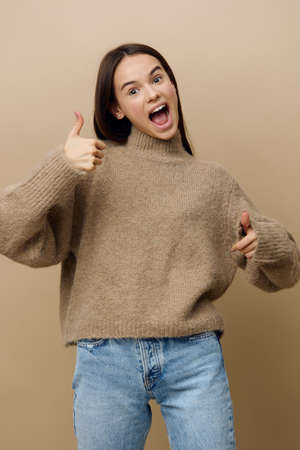 a happy, joyful woman stands on a beige background and vividly expresses emotions by giving a thumbs...