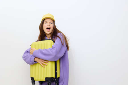 outraged, the woman stands on a white background in a purple tracksuit and a yellow cap, she gripped the suitcase with both hands with disdain, looking at the frontの写真素材